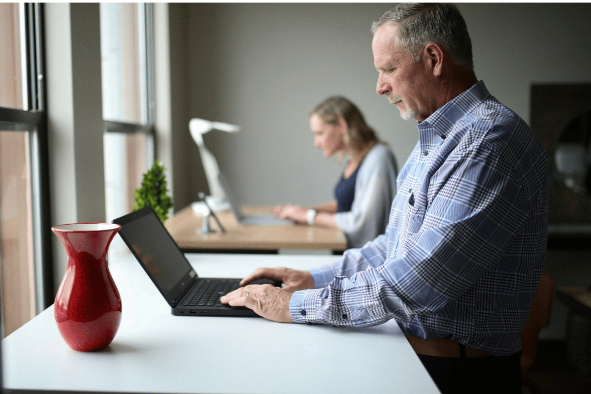 Two office workers seated at laptops demonstrating forward head posture and desk-related upper back tension associated with pec minor tightness and thoracic stiffness