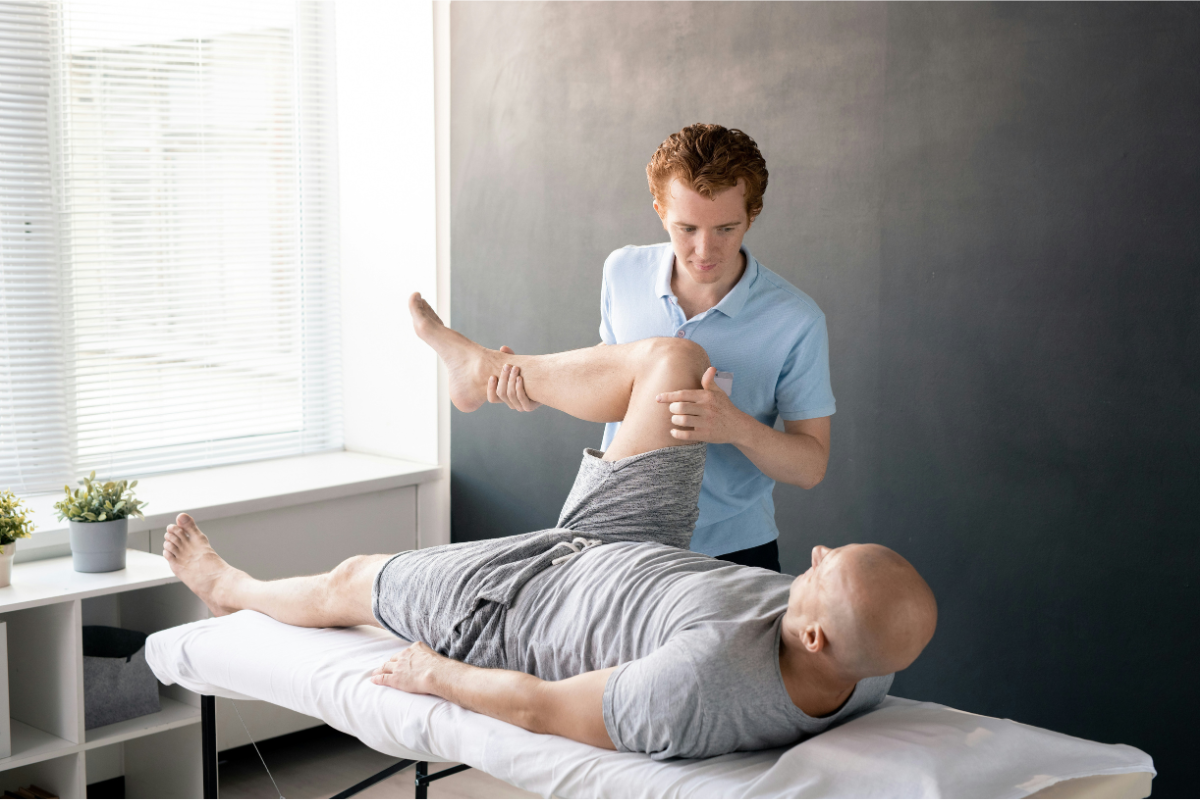 Physical therapist performing manual soft tissue therapy on a prone patient's anterior thigh and quadriceps to address knee, hip, and gait mobility restriction