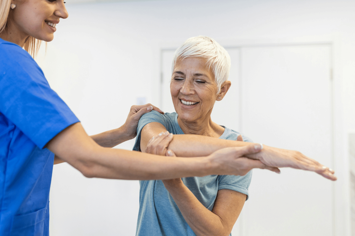 Clinician guiding an older patient through an arm and shoulder movement in a clinic, illustrating professional soft tissue and mobility care