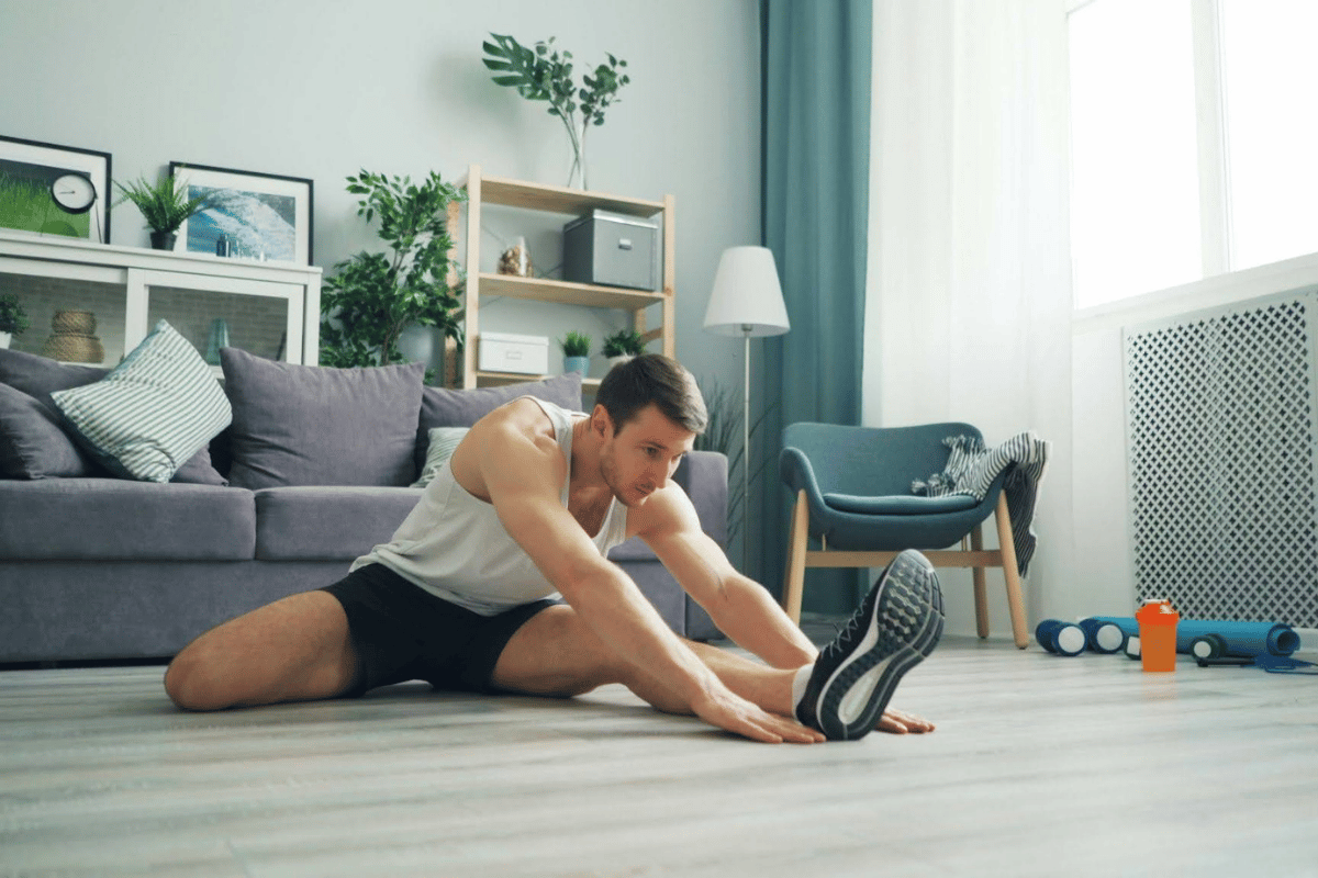 Man stretching his hamstring on the floor at home, part of a simple muscle recovery routine after a workout.