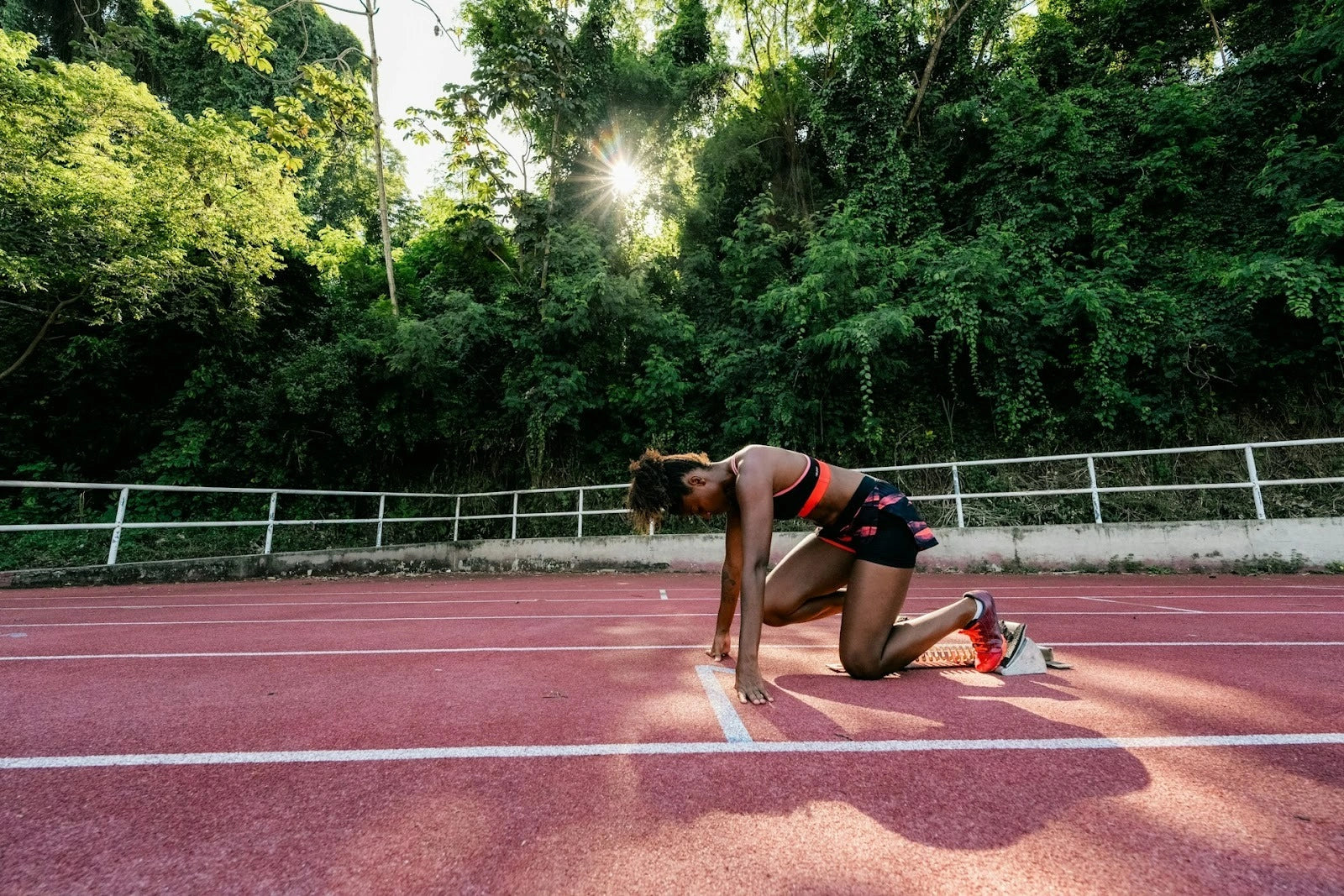 Female athlete in a starting position on an outdoor track, preparing to sprint, highlighting forefoot mechanics and big-toe loading relevant to bunion assessment and rehabilitation.