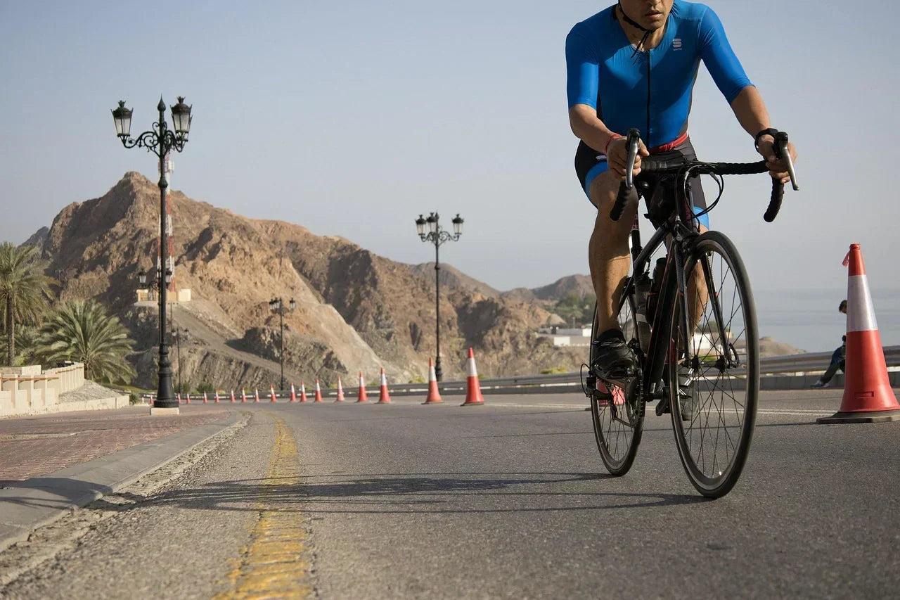 Cyclist riding on a road through a mountainous landscape, emphasizing foot alignment and continuous forefoot loading relevant to hammertoe development and prevention.