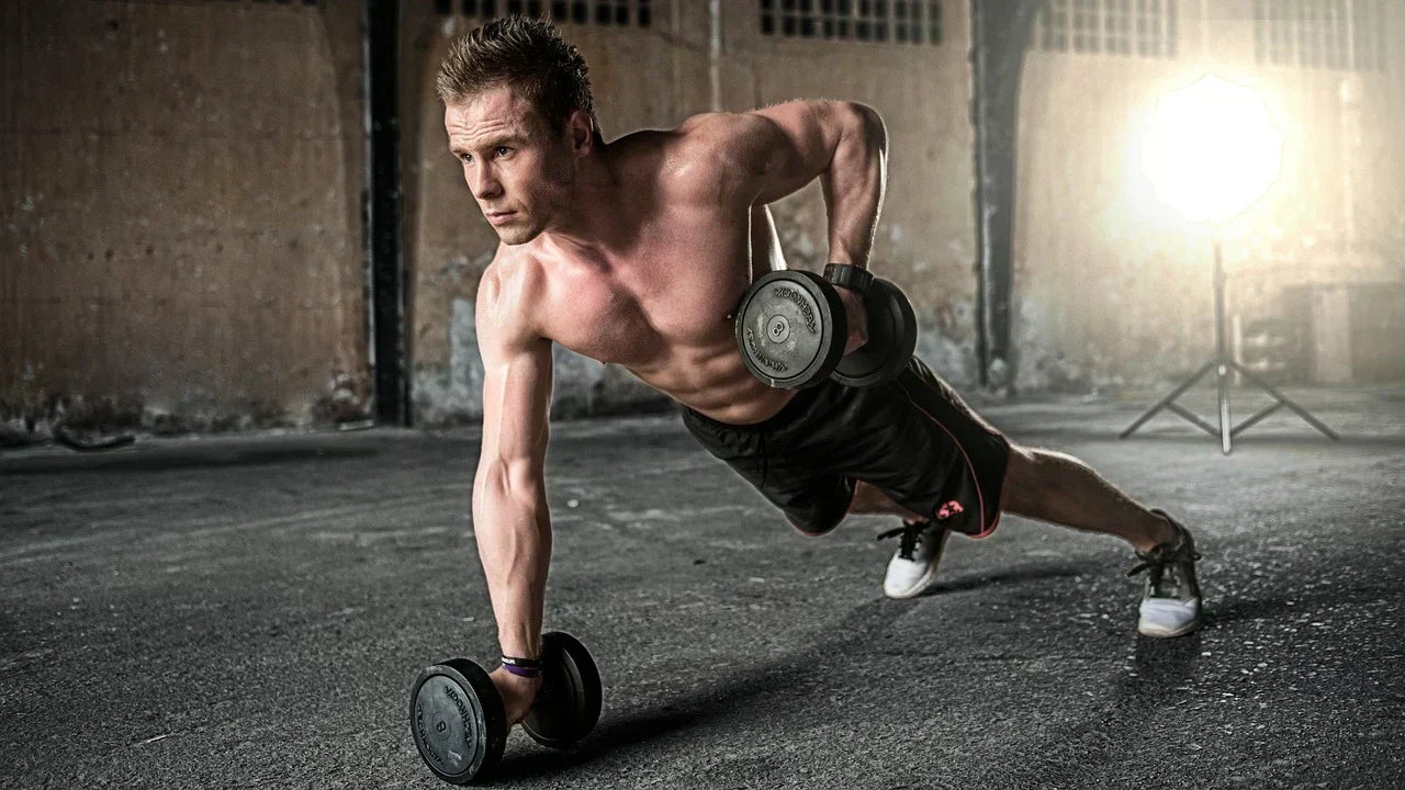 Male athlete performing dumbbell plank rows in an industrial gym setting, demonstrating strength, stability, and core engagement,  emphasizing the importance of strong feet and balanced training for athletic performance and flat foot recovery.