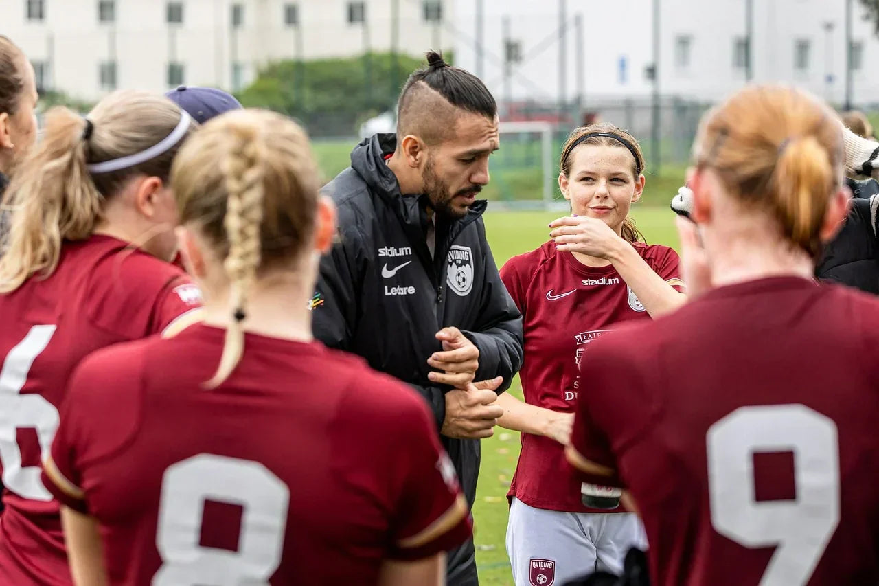 Coach speaking to a group of female athletes during soccer practice, emphasizing performance, foot health, and recovery strategies for managing heel pain and plantar tension.