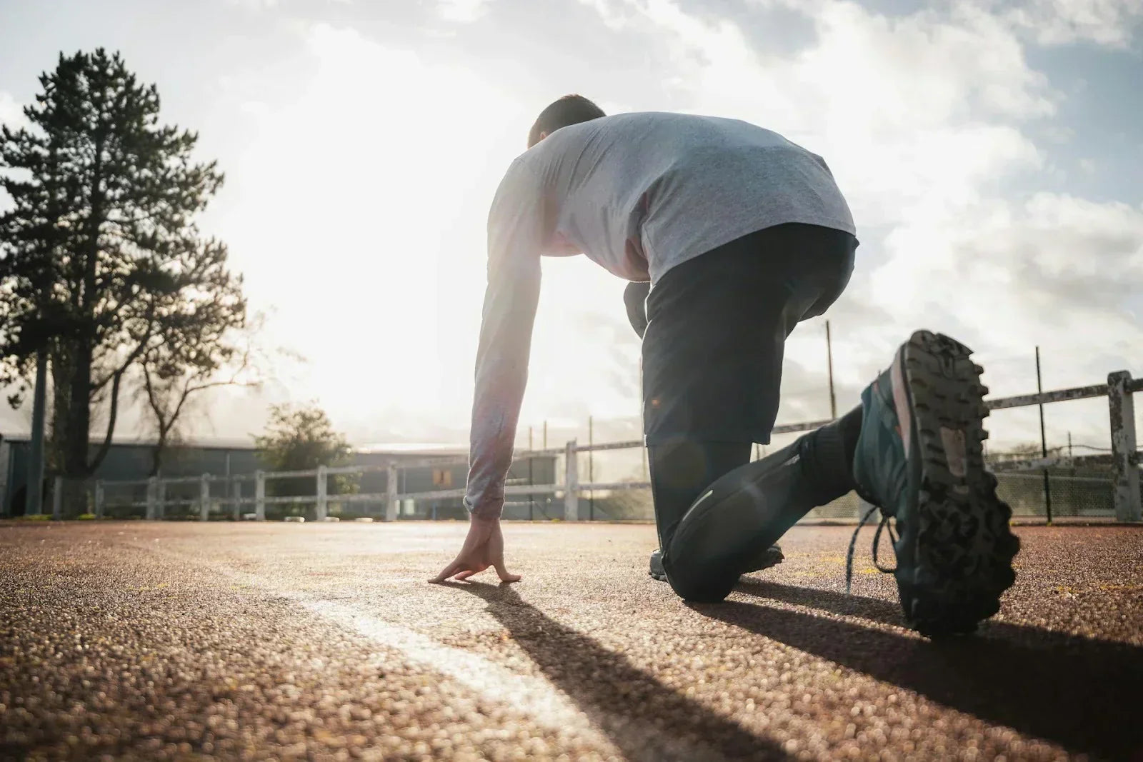 Athlete in a starting position on an outdoor track at sunrise, symbolizing movement, performance, and recovery-focused mobility practices.