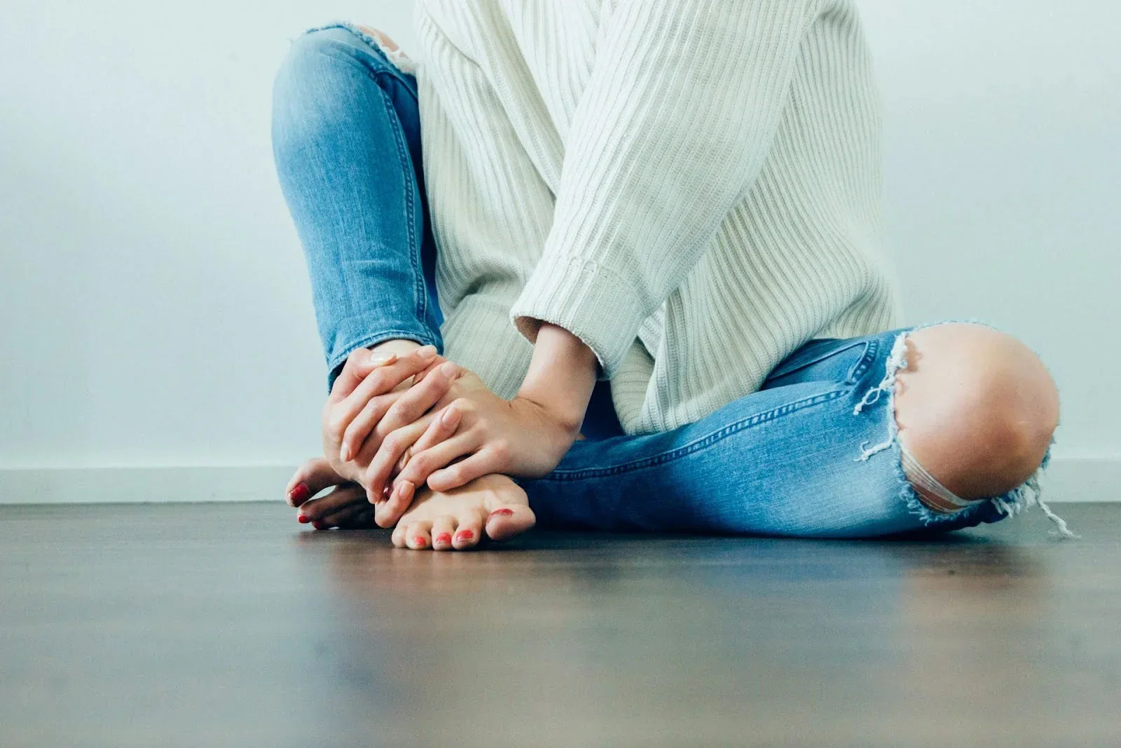 Person sitting cross-legged on the floor holding their foot, symbolizing foot discomfort and at-home recovery strategies for peripheral neuropathy relief and circulation support.