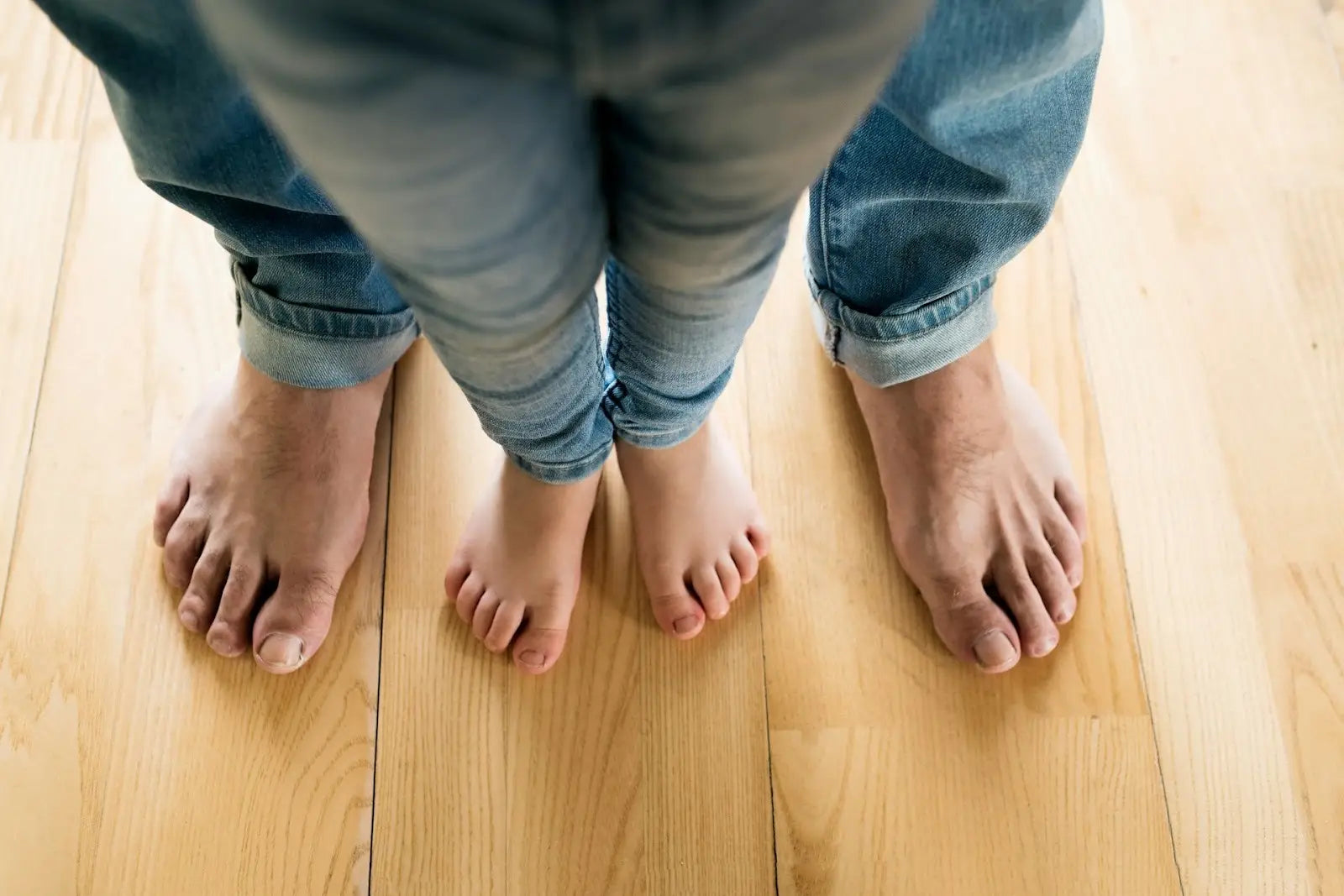 Adult and child standing barefoot together on a wooden floor, symbolizing balance, foot strength, and the role of big toe function in daily comfort and mobility.