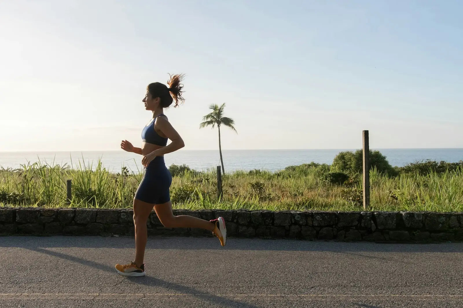 Woman jogging outdoors along a coastal path, illustrating the movement demands of prolonged running and the influence of repetitive ground forces on lower-body endurance.