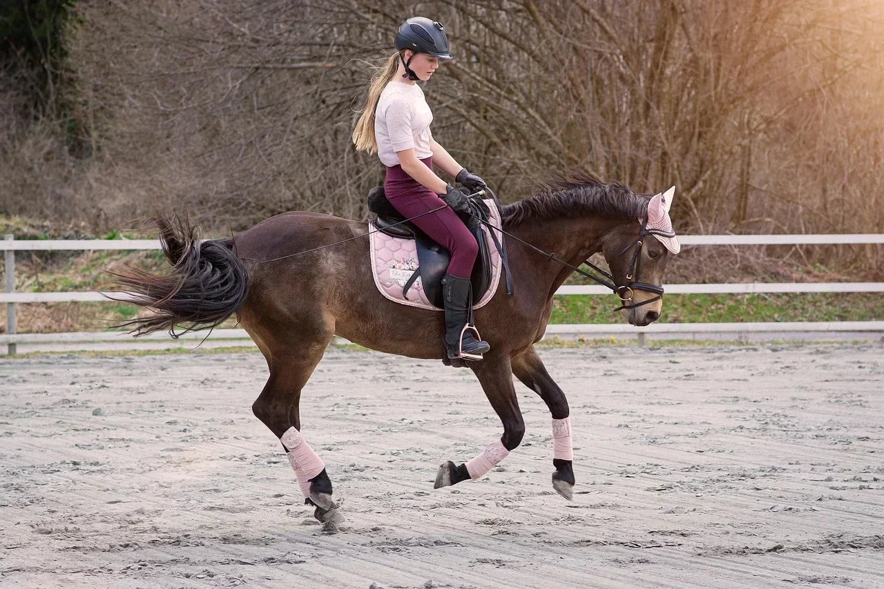 Equestrian athlete riding a horse in an outdoor arena, demonstrating lower-leg loading, foot positioning, and full-body mechanics relevant to understanding foot strain under increased body or activity load.