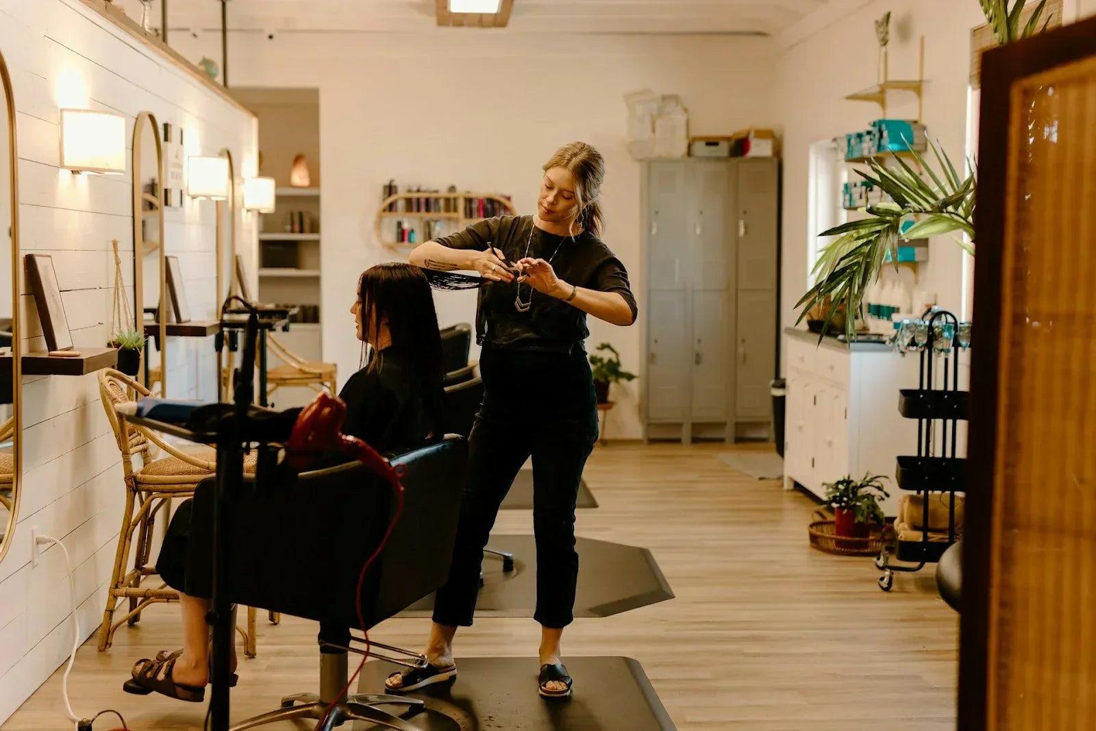 Hairstylist standing for long hours while cutting a client’s hair, demonstrating how prolonged standing and added body load increase foot strain and lower-leg fatigue.