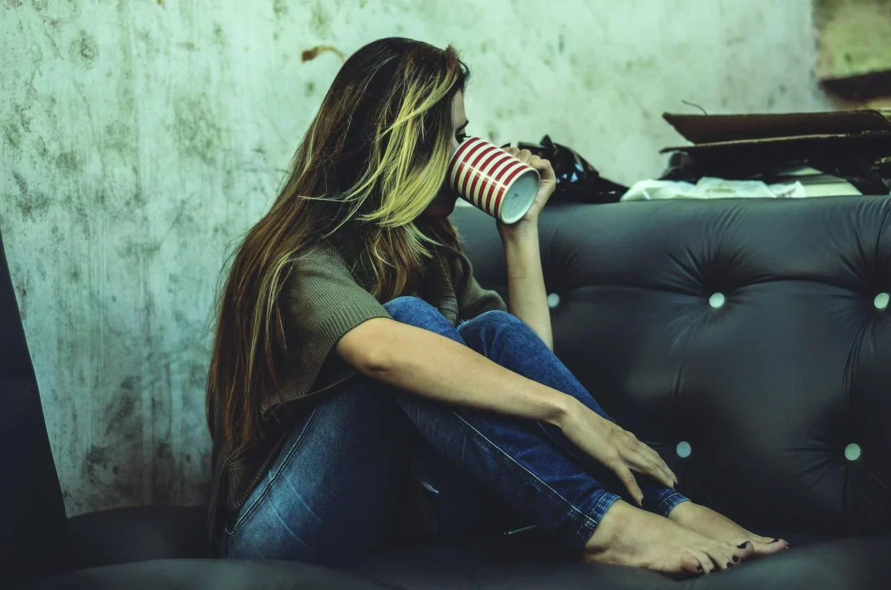 Woman sitting on a couch with her legs folded and barefoot, showing relaxed feet and natural toe alignment while drinking from a striped mug.