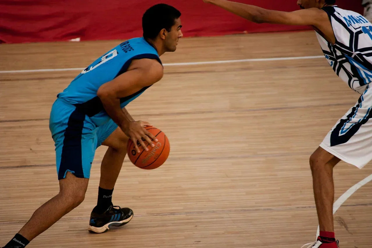 Basketball player in a low athletic stance while dribbling, highlighting foot and ankle loading, rapid direction changes, and movement demands relevant to Tarsal Tunnel Syndrome risk in athletes.